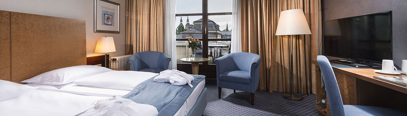 Elegant superior room at Maritim Hotel Fulda with double bed, seating area, and balcony overlooking the city.