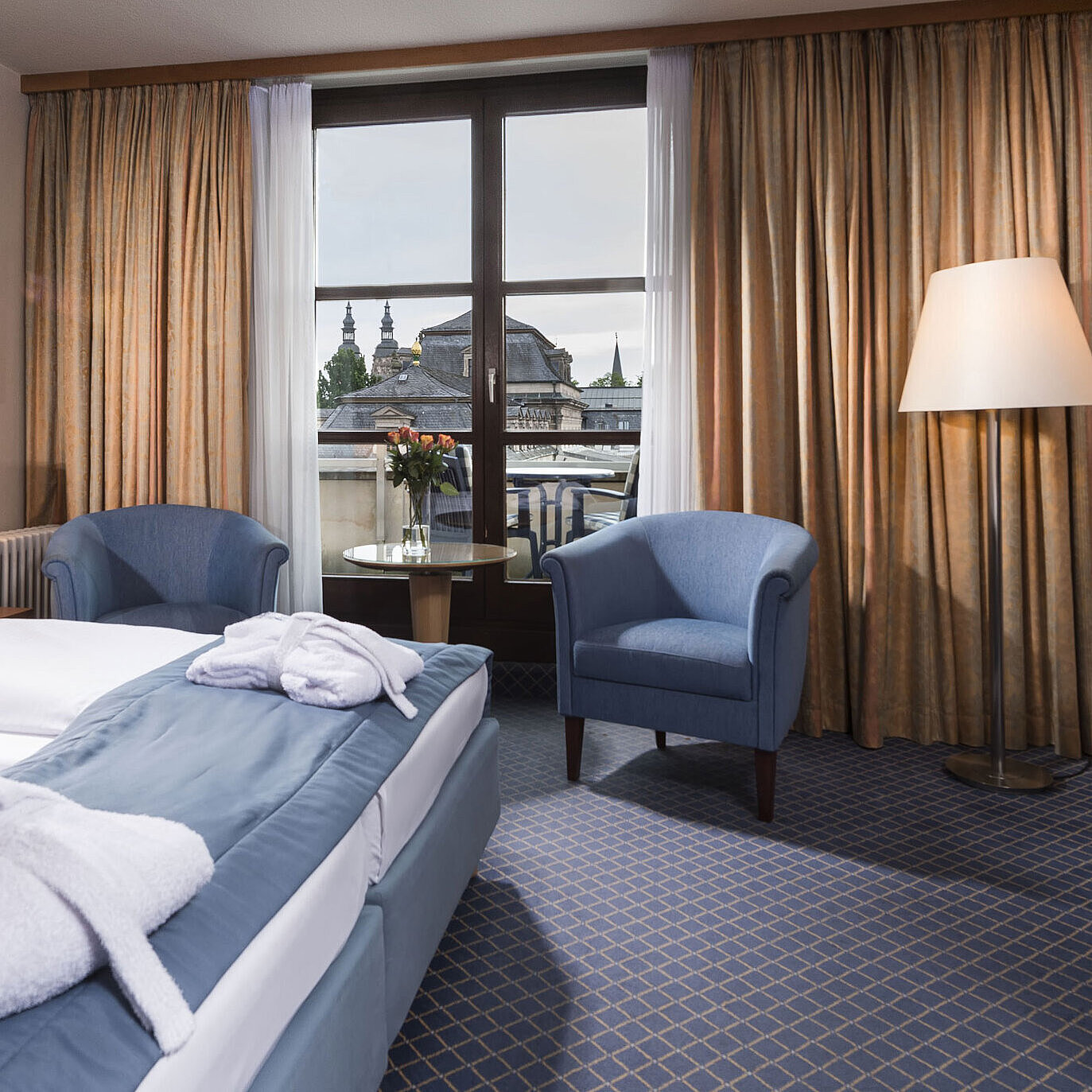 Elegant superior room at Maritim Hotel Fulda with double bed, seating area, and balcony overlooking the city.
