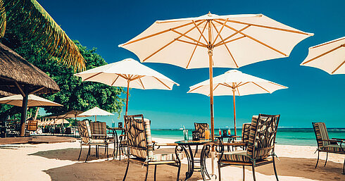 Beach restaurant with tables, chairs and parasols directly by the turquoise sea