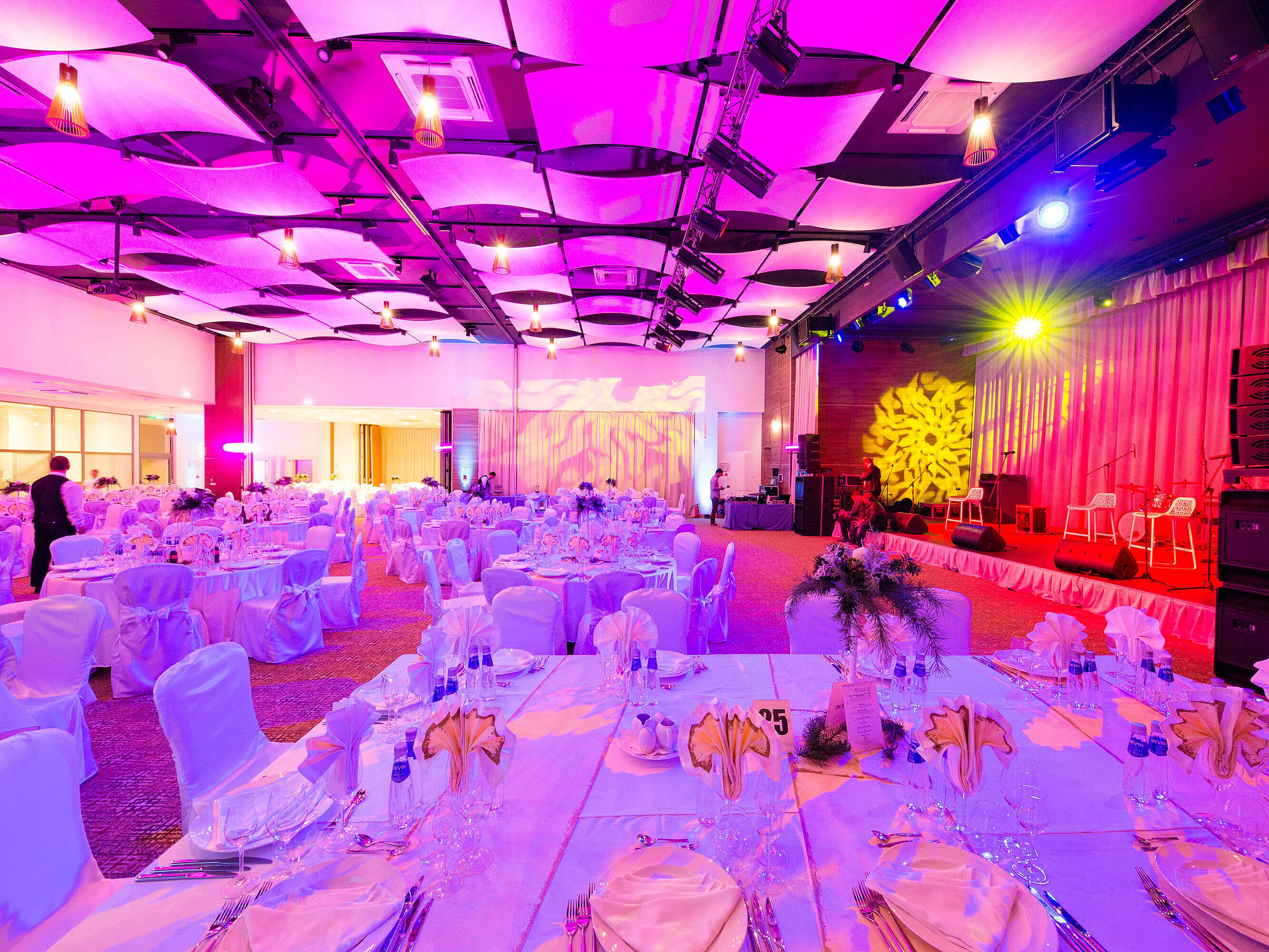 Large banquet hall with decorated tables, stage and vibrant event lighting