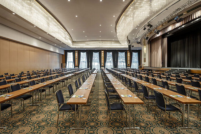 Magnificent hall at the Maritim Hotel Magdeburg with a stage, row seating, and luxurious chandelier.