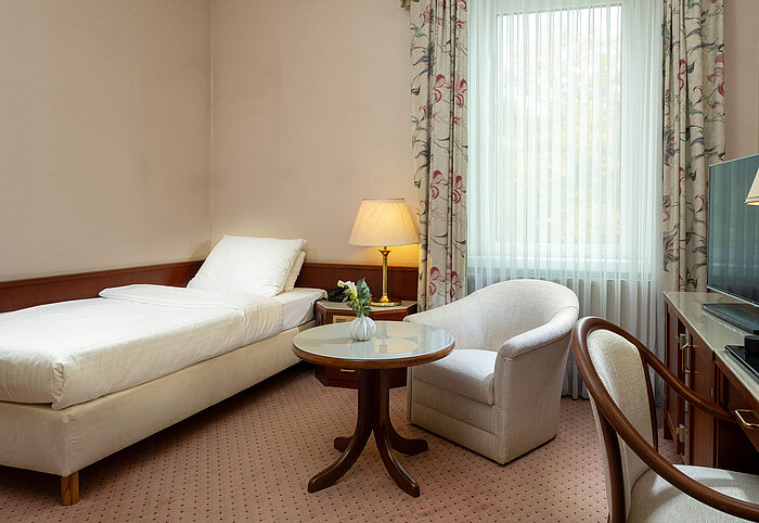 Classic single room with bed, seating area, desk and large window in bright traditional design at Maritim Hotel Bad Wildungen.