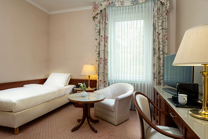 Classic single room with bed, seating area, desk and large window in bright traditional design at Maritim Hotel Bad Wildungen.