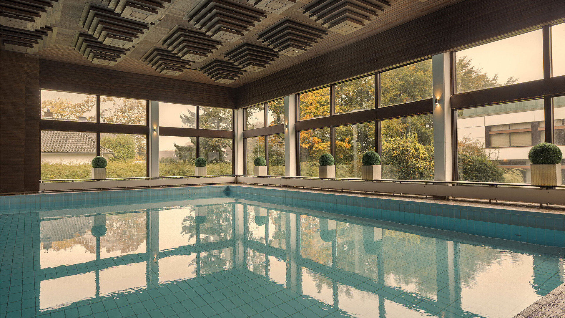 Indoor pool at the Maritim Hotel Kiel, surrounded by large windows offering a view of the greenery.