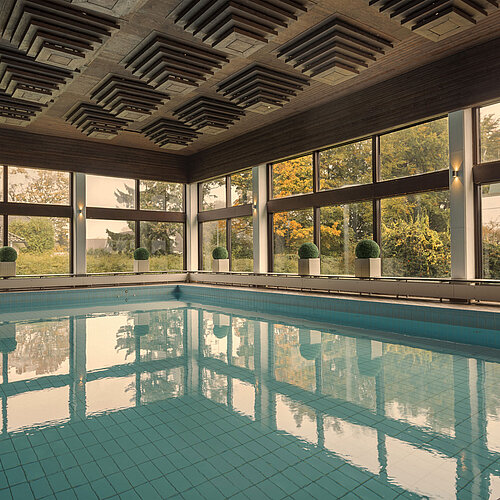 Indoor pool at the Maritim Hotel Kiel, surrounded by large windows offering a view of the greenery.