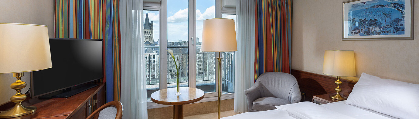 Classic room at Maritim Hotel Cologne with a double bed, desk, and view of the Rhine and historic city center.