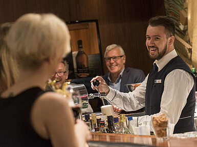 Friendly bartender serves a drink at the bar of Maritim Hotel Bad Salzuflen with smiling guests