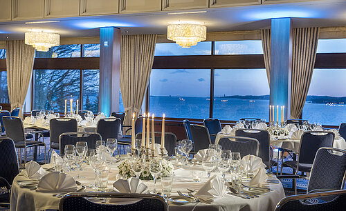 Maritim Hall in the Maritim Hotel Kiel, festively laid tables with candlelight, large windows and sea views at dusk