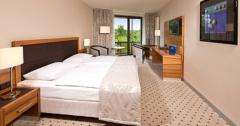 Bright room at Maritim Hotel Bad Homburg with cozy bed, desk, and balcony with green view.