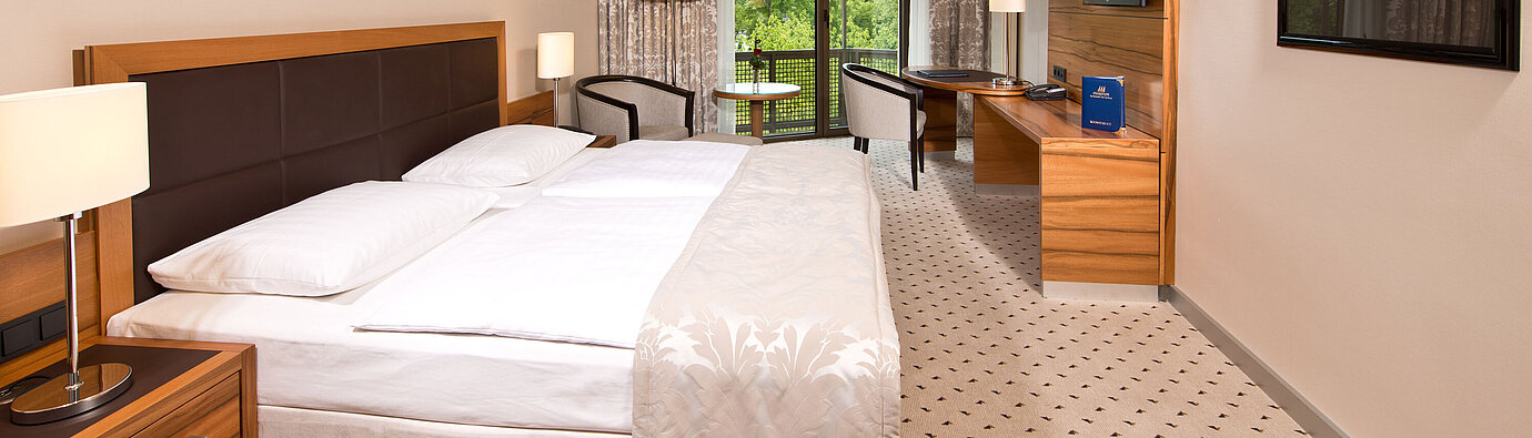 Bright room at Maritim Hotel Bad Homburg with cozy bed, desk, and balcony with green view.