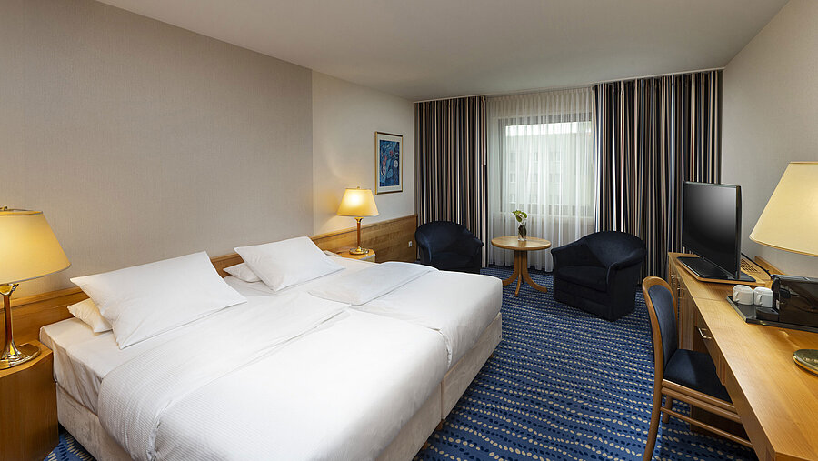 Large bed with bedside tables and lamps, next to seating area and desk.