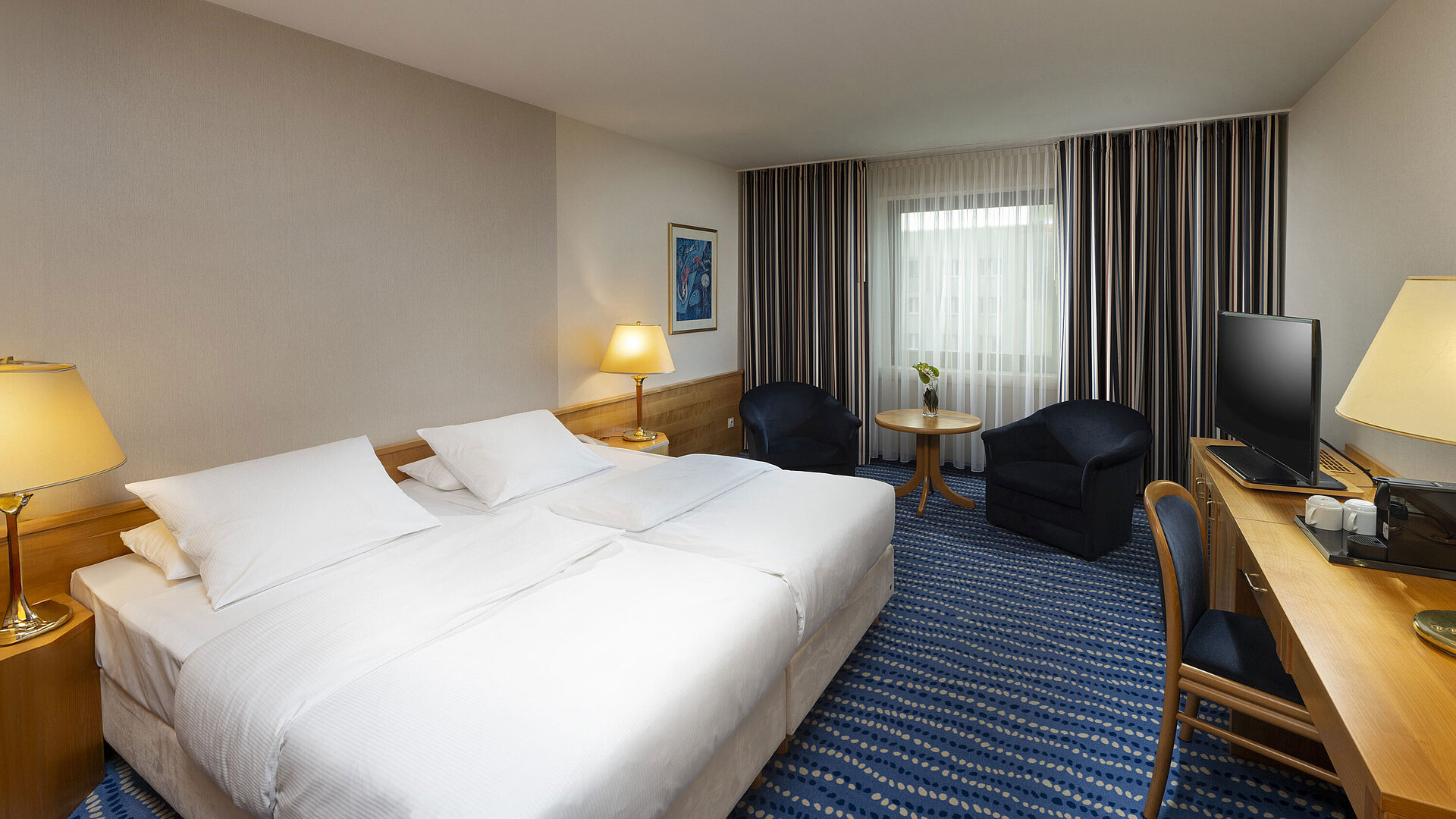 Large bed with bedside tables and lamps, next to seating area and desk.