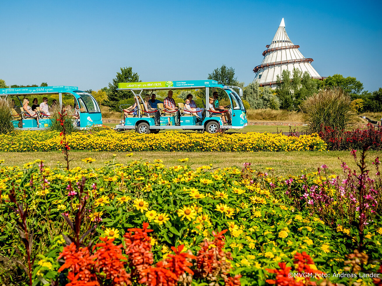 Elbe-Express train passing colorful flower beds in Elbauenpark Magdeburg with the Millennium Tower in the background