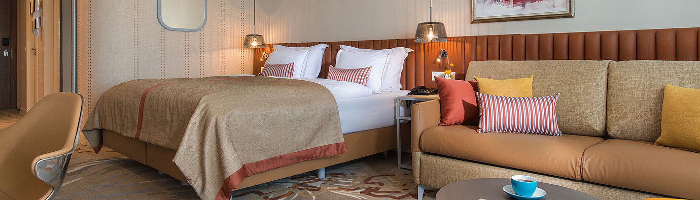 Modern room at Maritim Hotel Amelia with large bed, cosy sofa and warm colour accents