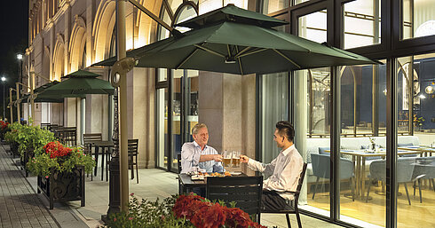 Guests clinking beers on the illuminated hotel restaurant terrace in the evening