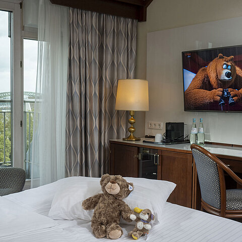 Family room at the Maritim Hotel Cologne with TV, cozy stuffed animals on the bed, and a view of the Rhine.