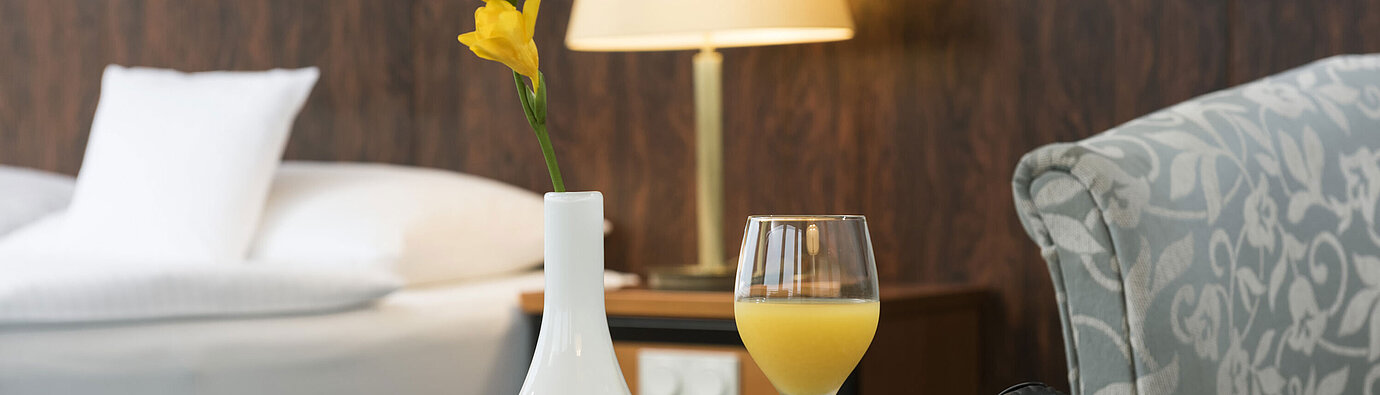 Detail of the hotel room Details of a room at the Maritim Hotel Kiel: glass of orange juice, headphones and vase on the table, a bed in the background.