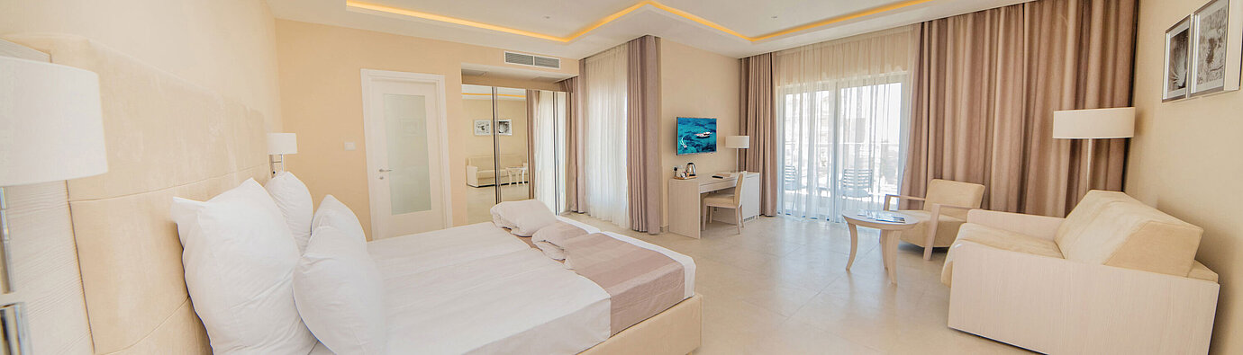 Bright double room with large bed, seating area, desk and balcony window in a modern, elegant design