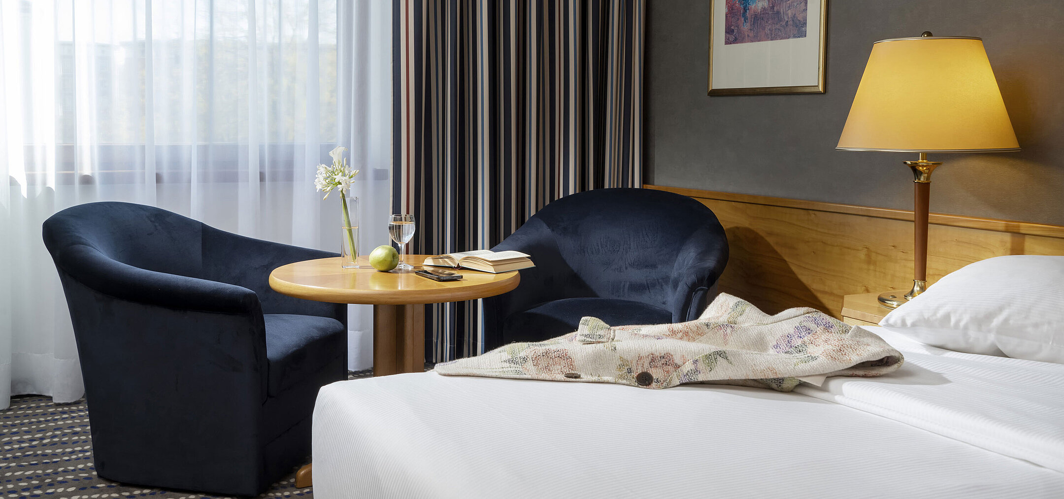Seating area in hotel room with table, book, glass of water, and apple, perfect for relaxing
