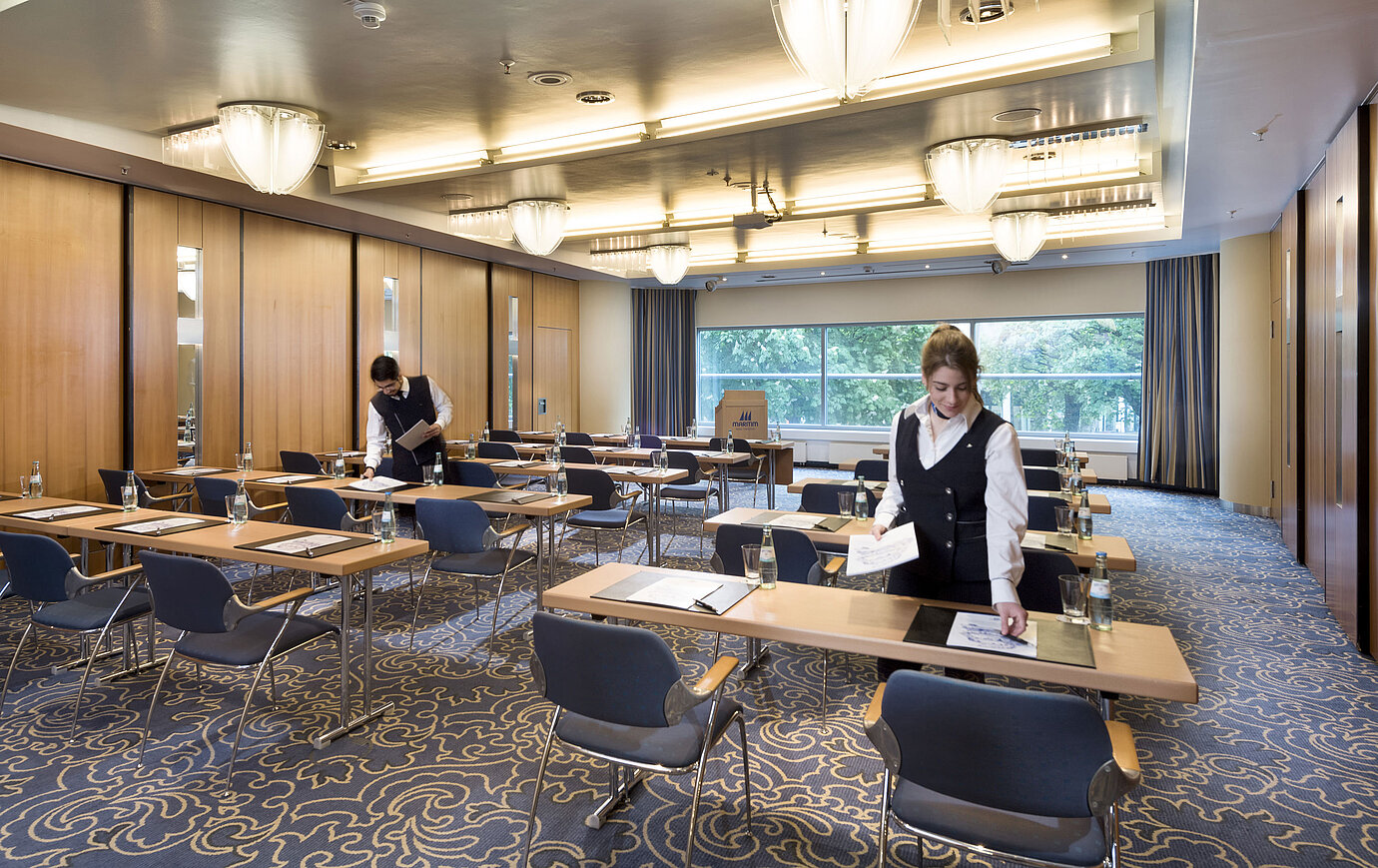 Staff preparing a conference room at Maritim Hotel Frankfurt with row seating and views of greenery.