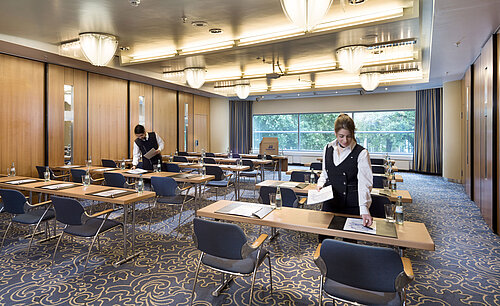 Staff preparing a conference room at Maritim Hotel Frankfurt with row seating and views of greenery.