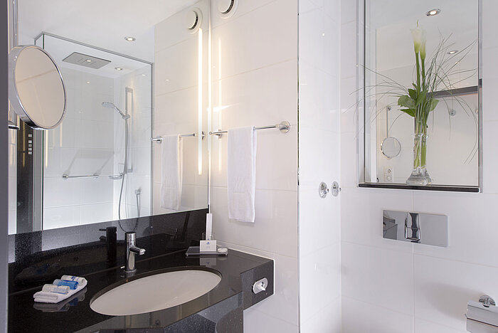 Bright bathroom with glass shower, mirror and black counter at the Maritim Hotel Munich