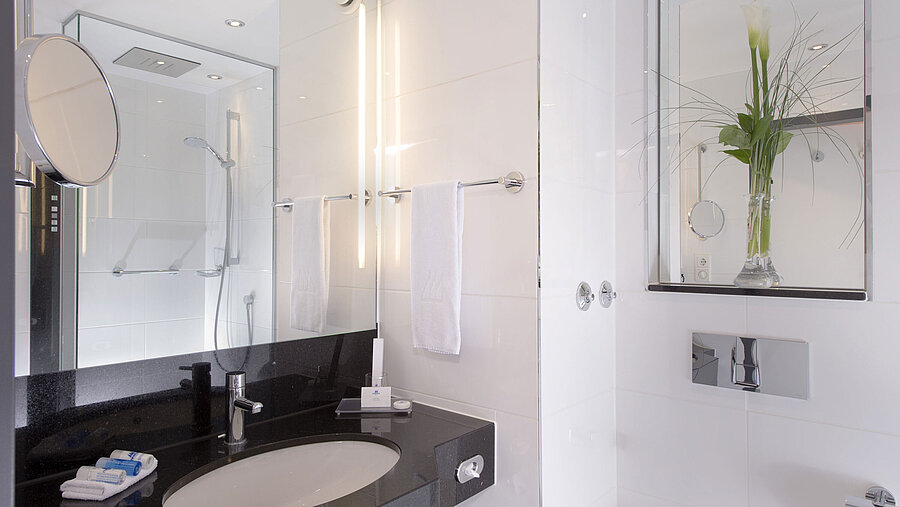 Bright bathroom with glass shower, mirror and black counter at the Maritim Hotel Munich