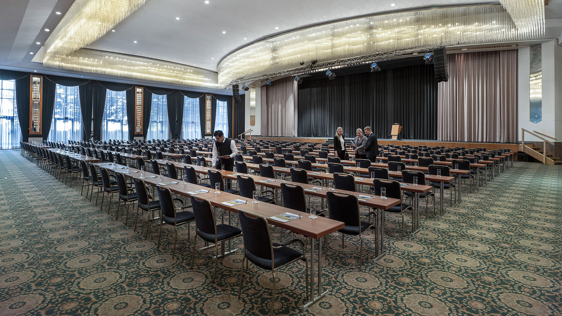 Magnificent hall at the Maritim Hotel Magdeburg with a stage, row seating, and luxurious chandelier.