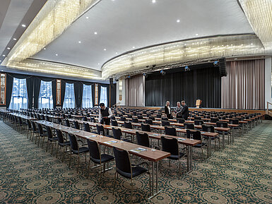 Magnificent hall at the Maritim Hotel Magdeburg with a stage, row seating, and luxurious chandelier.