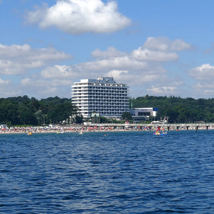 Maritim Seehotel Timmendorfer Strand, pier, and colorful flags from a boat on a sunny day.