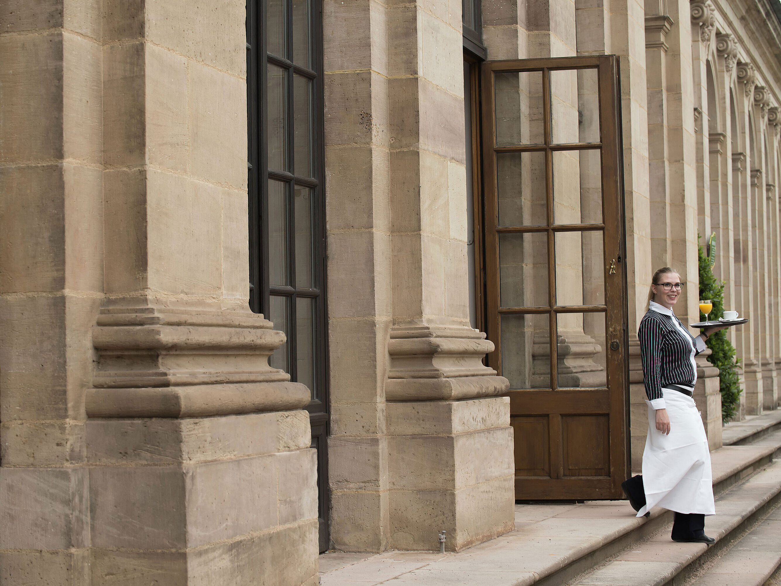 Friendly waitress serving breakfast with freshly squeezed orange juice on the terrace of Maritim Hotel Fulda.