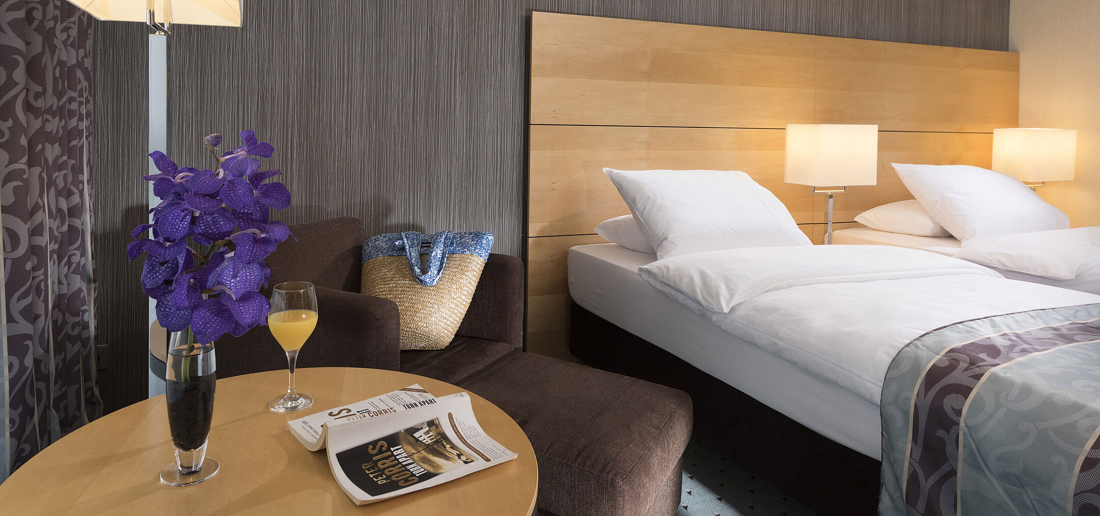 Classic room at Maritim Hotel Düsseldorf with elegant double bed, cozy seating area, fresh flower, and reading material.