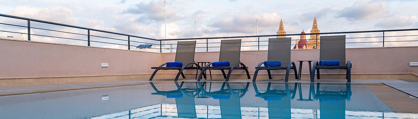 Rooftop pool with sun loungers and city views under a blue sky