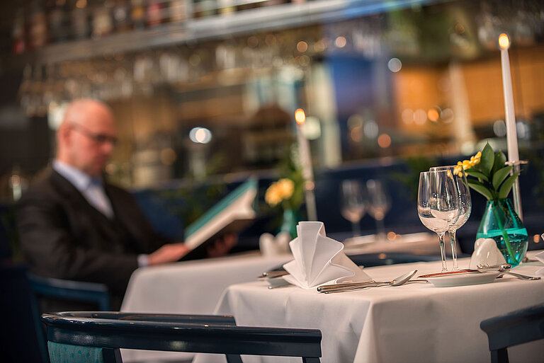 Elegant set table in the restaurant of Maritim Hotel Magdeburg with a guest looking at the menu.