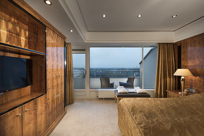 Penthouse bedroom with wooden furniture, large windows, and balcony view at Maritim Seehotel Timmendorfer Strand.