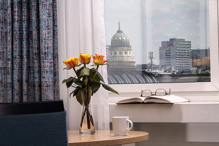 Vase with yellow roses, book and cup by window overlooking Französischer Dom at Maritim proArte Hotel Berlin