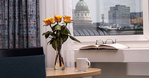 Vase with yellow roses, book and cup by window overlooking Französischer Dom at Maritim proArte Hotel Berlin