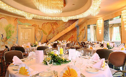 Elegant banquet hall with wall paintings, chandeliers and festively set tables