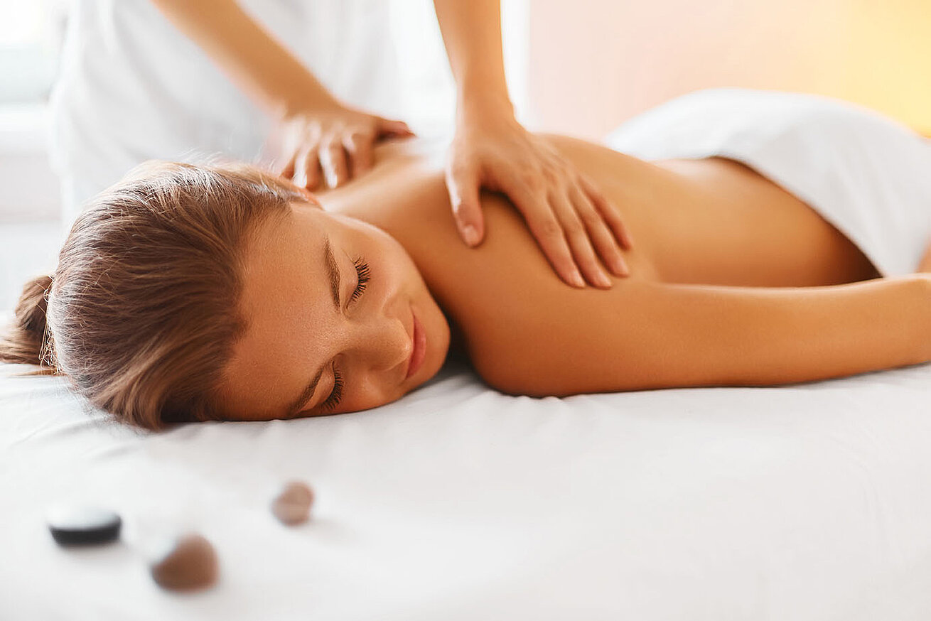 Woman enjoying relaxing back massage in spa with warm light and stones