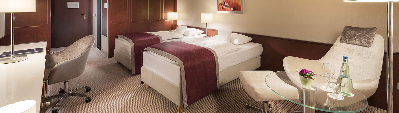 Comfort room at Maritim Hotel Bonn, featuring two single beds, armchair, desk, and modern lighting.