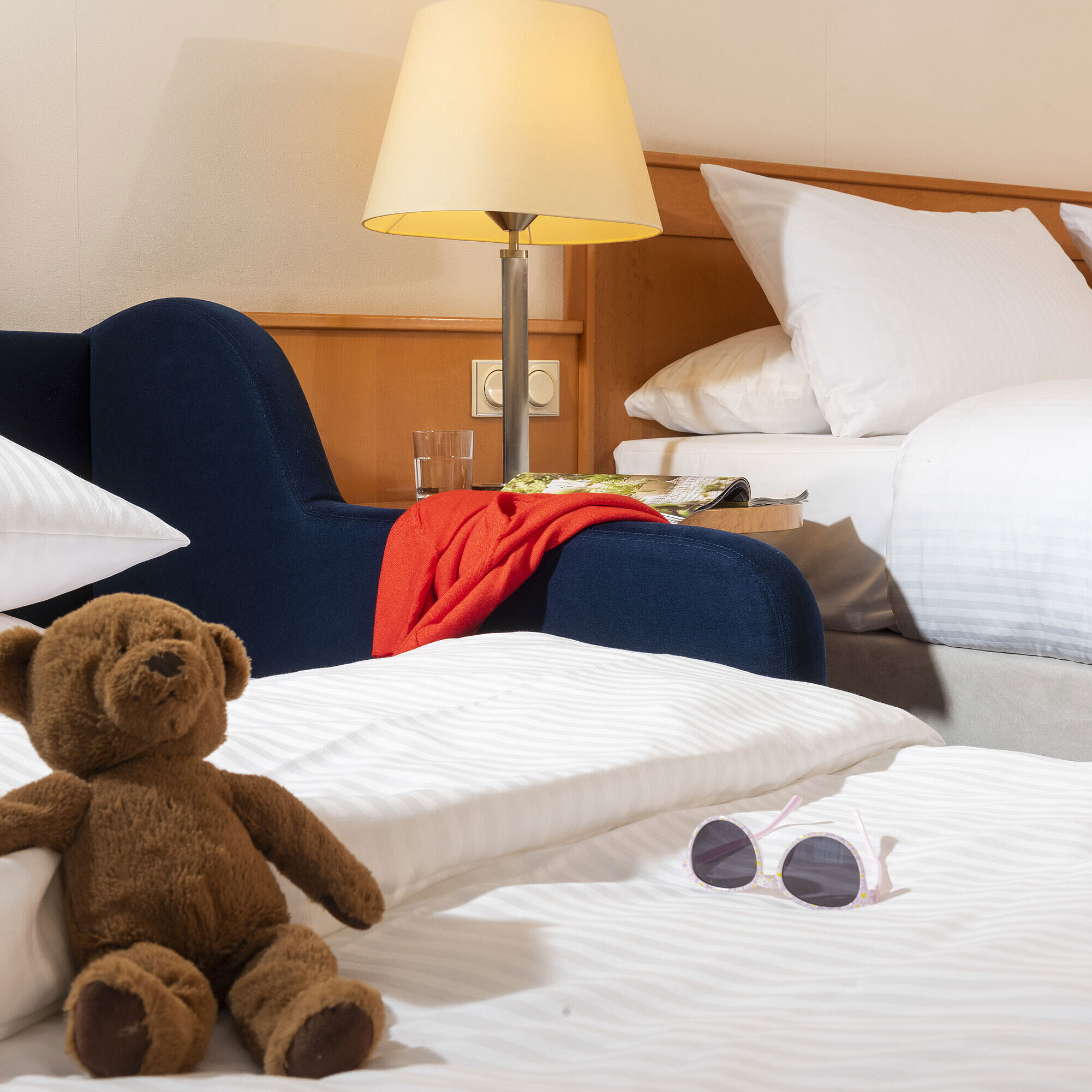 Cozy family room at Maritim Hotel Frankfurt with a teddy bear, sunglasses, and soft beds for a relaxing stay.