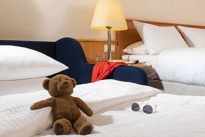 Cozy family room at Maritim Hotel Frankfurt with a teddy bear, sunglasses, and soft beds for a relaxing stay.