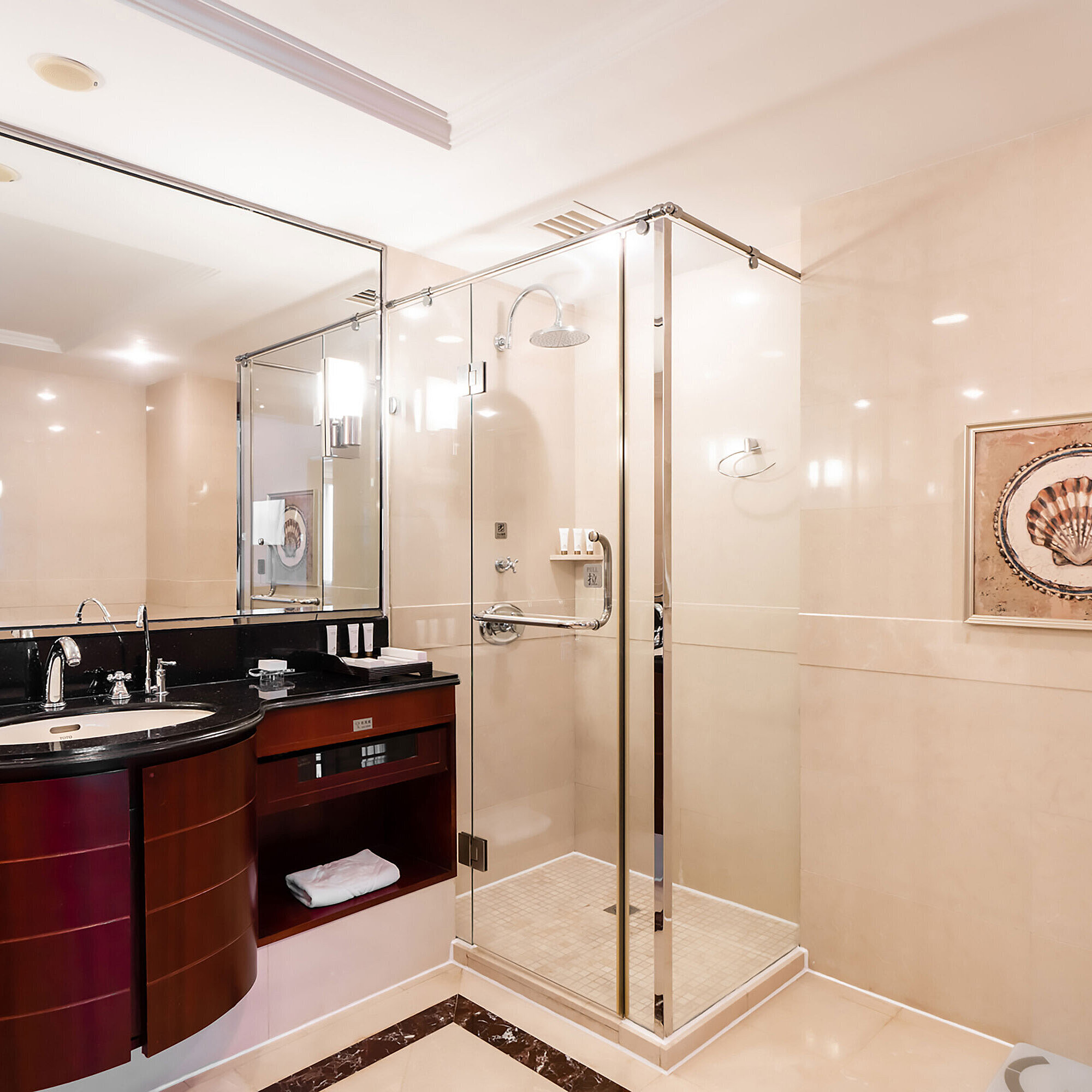 現代化酒店浴室配備玻璃淋浴間、大型鏡子、黑色梳妝台，牆面裝飾著貝殼藝術品