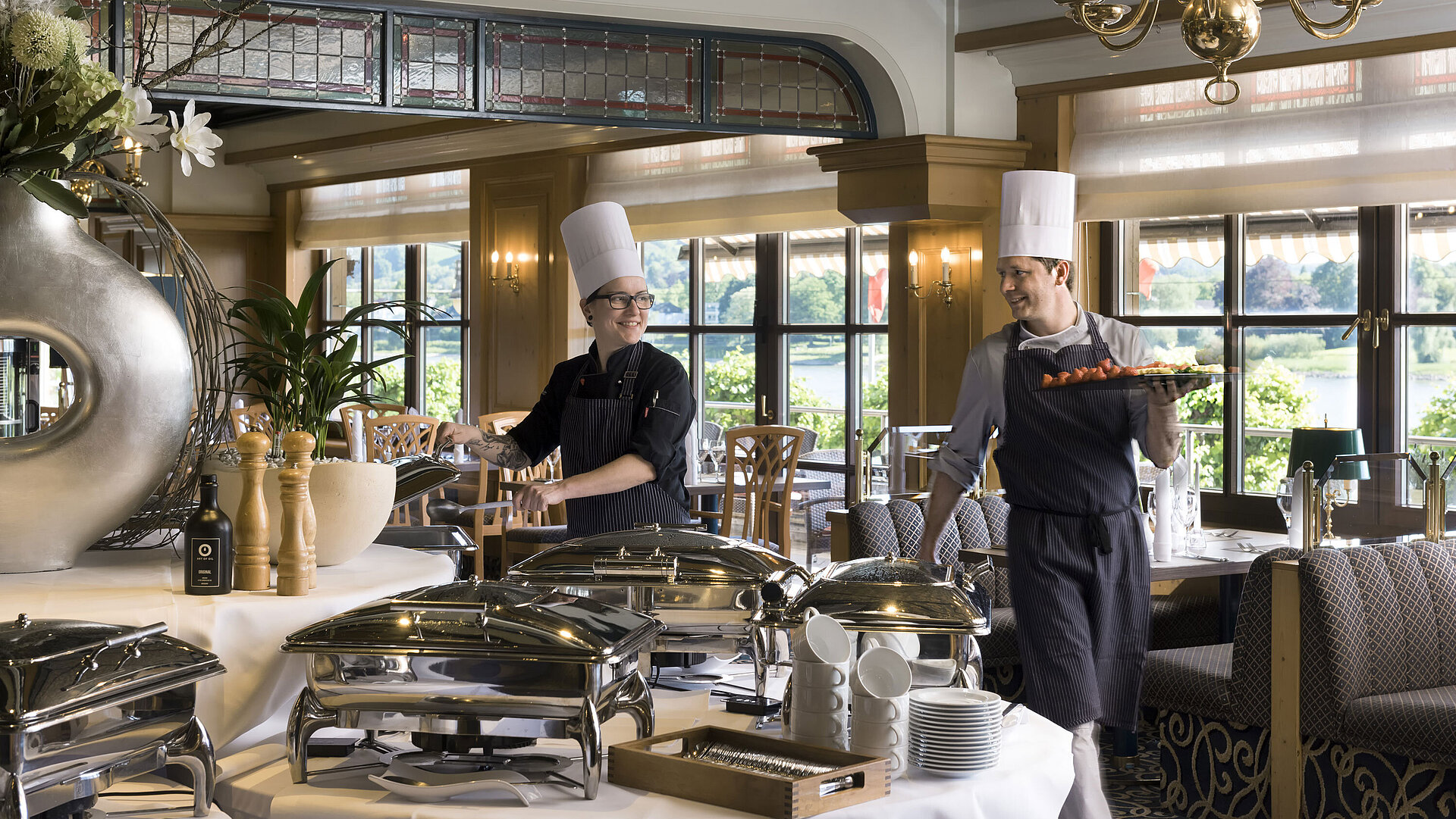 Two chefs at the buffet in Maritim Hotel Königswinter preparing freshly arranged dishes with a view of the Rhine.