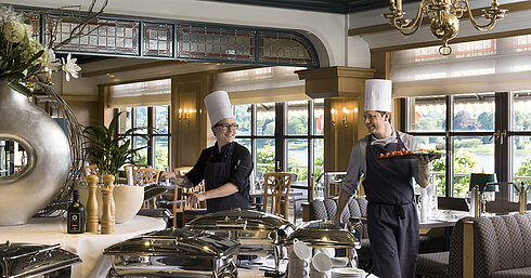 Two chefs at the buffet in Maritim Hotel Königswinter preparing freshly arranged dishes with a view of the Rhine.