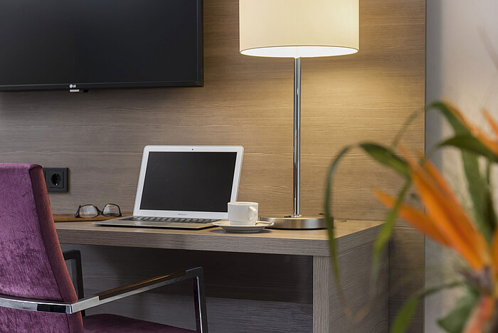 Desk at Maritim Hotel Königswinter with laptop, reading glasses, and elegant table lamp.