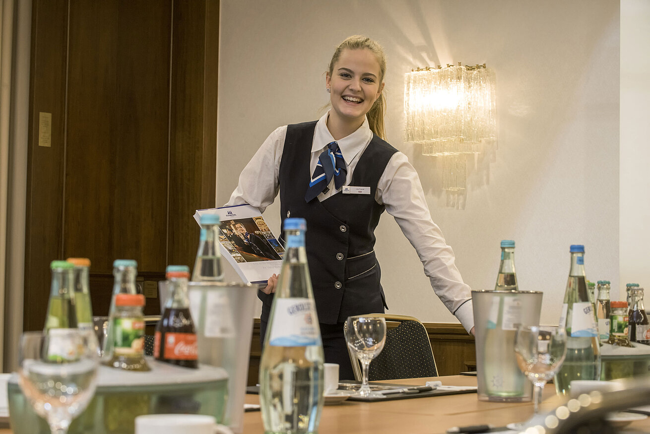 Friendly service employee in the Salon Lenné of the Maritim Hotel Bonn with drinks and conference documents on the table.