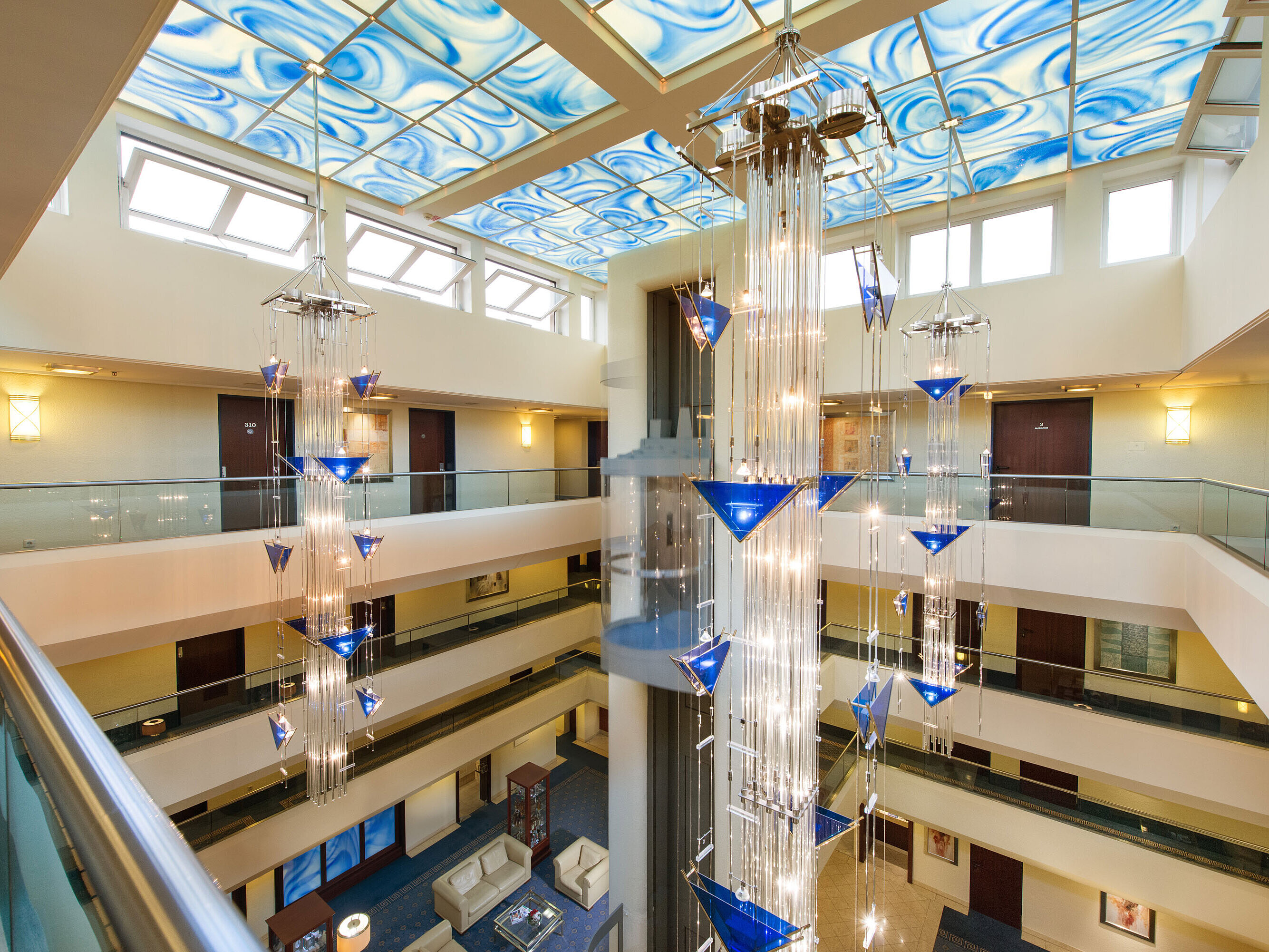 Modern atrium at Maritim Hotel Fulda with glass elevator, blue ceiling design, and artistic chandelier.