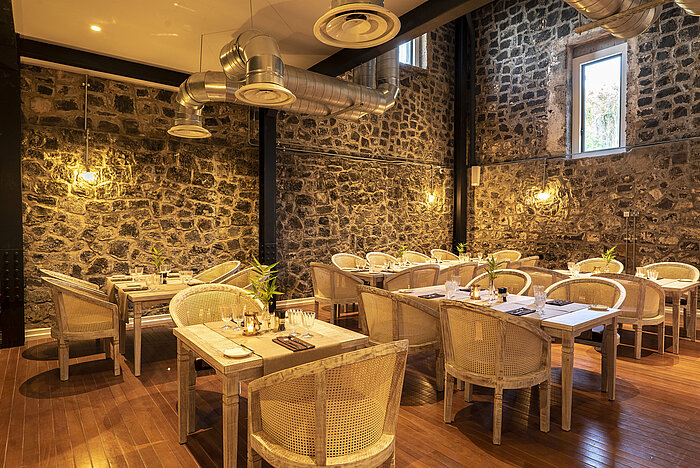 Modern restaurant interior with natural stone walls, wooden tables and visible ventilation system