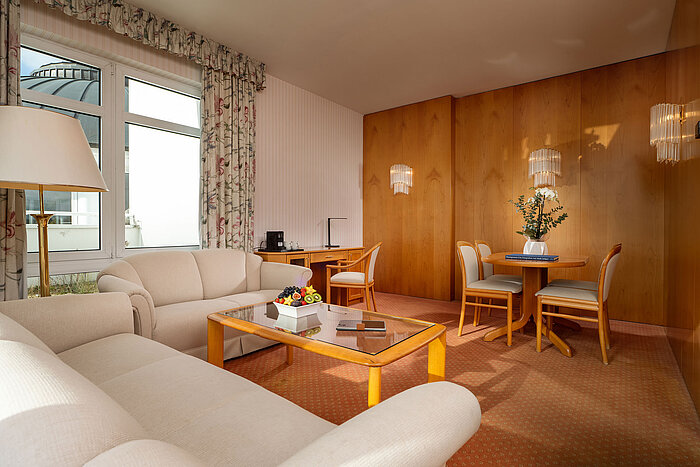 Junior Suite with bright living area, sofa, glass table, dining space and cosy interior at the Maritim Hotel
